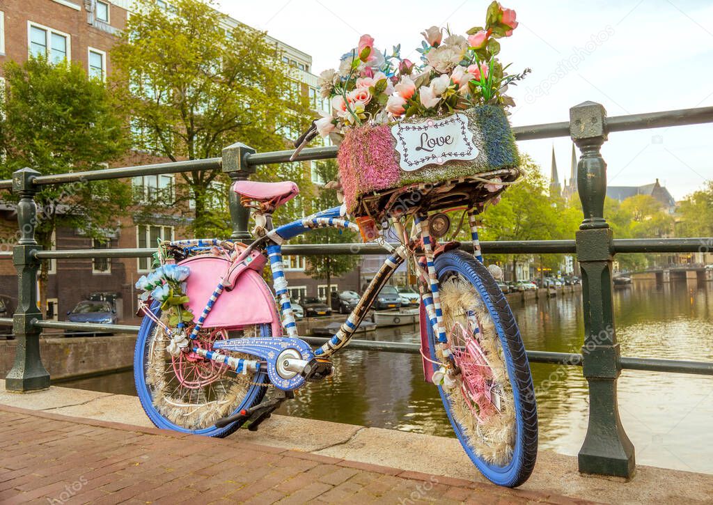Netherlands. Cloudy morning on the Amsterdam canal. A flower-decorated bicycle with a LOVE sign is parked by the bridge fence