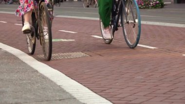 Amsterdam caddesinde bisiklet yolu. İki kız bisiklete biniyor. Sadece tekerlekler ve bacaklar görünür. Yavaş çekim