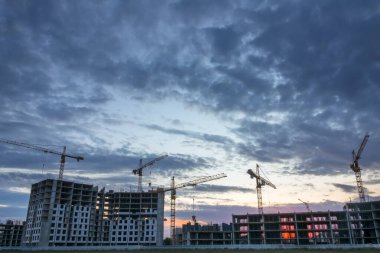 Yazın alacakaranlıkta konut inşaatında. Birçok vinç çalışıyor.