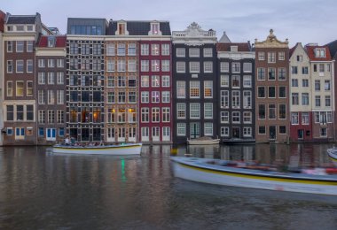 Hollanda 'da. Alacakaranlıkta Amsterdam 'da klasik kanal evleri. Turist tekneleri