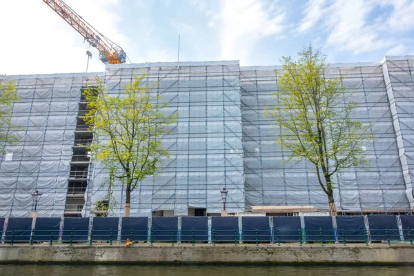 Nice splash screen for a site under construction! Netherlands. Renovation of a multi-storey building on the canal embankment and a crane. The entire facade is covered with scaffolding and dust curtains