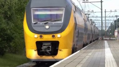Hollanda 'da. İki çift katlı banliyö treni kırsal bir tren istasyonunun yanından geçiyor.