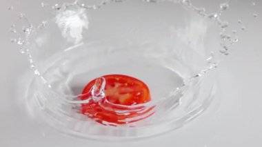 İnce katmanlı beyaz bir masa. Bir dilim sulu domates düşer ve bir sürü sıçrama yaratır. Yavaş çekim