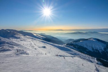 Slovakya. Kış kayak merkezi Jasna. Mavi gökyüzünde parlak güneş kayak yamacının üzerinde. Ufuktaki dağ zirveleri ve sis