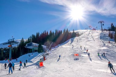 Slovakya, Jasna - 5 Şubat 2019 kış kayak merkezi Jasna. Kayak yamacının üstündeki mavi gökyüzünde parlak güneş. Kayak asansörleri ve birçok kayakçı