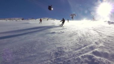 Slovakya. Jasna Kayak Merkezi. Güneşli hava ve kar fırtınası. Kayakçılar kayak yokuşundan aşağı inerler. Yavaş çekim