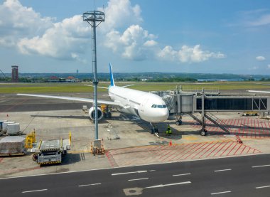 Endonezya havaalanında güneşli bir gün. Yolcu indirmek ve binmek için bağlı bir jet köprüsü olan bir uçak. Arka planda okyanus ve orman