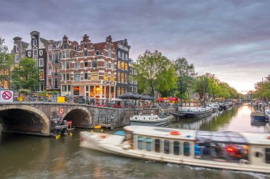 Hollanda 'da. Amsterdam Kanalı 'nda bulutlu bir alacakaranlık. Yüzen evler ve tekneler demirli. Geleneksel evlerin sularında yansıma ve bir köprü