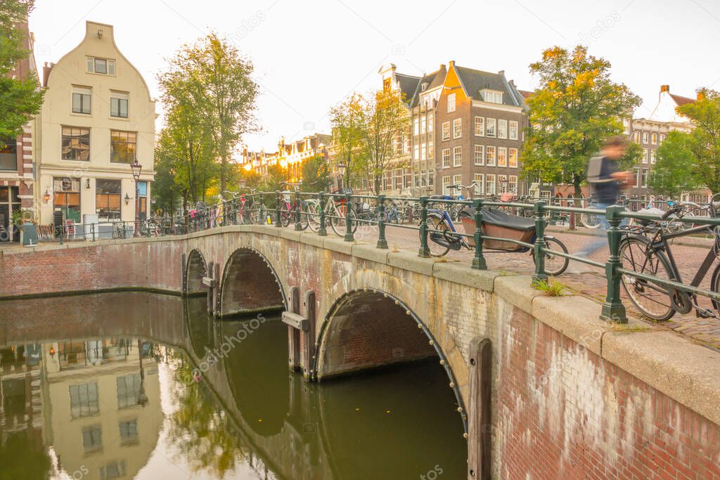 Netherlands. Stone bridge with three arches on the Amsterdam canal. Lots of parked bikes. Morning with the first rays of the sun
