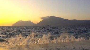 Yunanistan. Rion-Antirion köprüsünün yakınında gün batımı. Bir kırılma dalgası beton iskeleye çarpar. Yavaş çekim