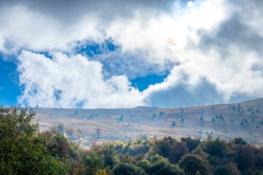 Yaz Ukraynalı Karpatlar. Gökyüzündeki bulutlar ve güneş ışığı bir yamacı samanlıklarla aydınlatıyor