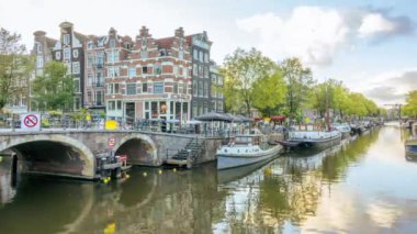 Netherlands. Summer evening at the crossroads of two canals in Amsterdam and typical buildings. Busy movement of boats on the water and cars, bicycles and people on the bridges. Time lapse