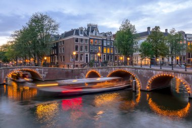 Netherlands. Summer evening on the canals of Amsterdam. Tourist boats sail under the bridges. Traditional houses and bicycles on the waterfront