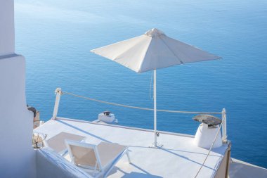 Greece. Terrace with sea view on a sunny day in Santorini. A pair of sun loungers and a sun umbrella