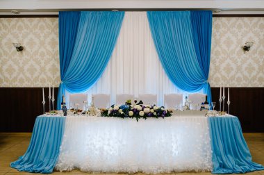 Şölen masası, kemer, çiçek ve yeşillik kompozisyonu ile süslenmiş, ziyafet salonundaki mumlar. Yeni evliler düğün ziyafeti alanında oturuyorlar. Modaya uygun bir düğün..