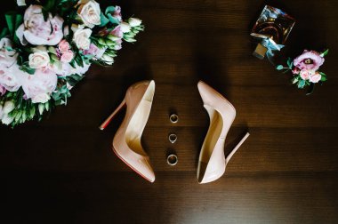 Pembe çiçeklerin, güllerin ve yeşilliklerin gelininin düğün buketi. Renkli, zarif klasik bej ayakkabılar, parfümler ve pastel arka planda duran altın yüzükler. Kapatın. Düz yat. en üstteki görünüm.