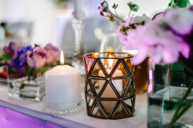 Menekşe, mor, pembe çiçekler ve yeşillik kompozisyonu ile süslenmiş şölen masası, şölen salonunda mumlar. Yeni evliler düğün ziyafeti alanında toplandı..