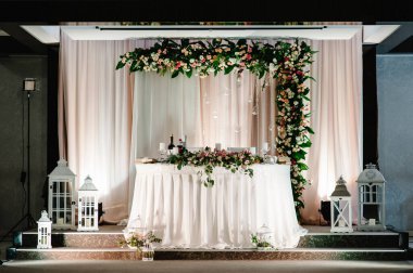 Şenlik masasında yeni evliler masa örtüsüyle kaplanmış çiçek ve yeşillik kompozisyonu ile süslenmiş düğün salonundaki mumlar. Çadırda düğün partisi.