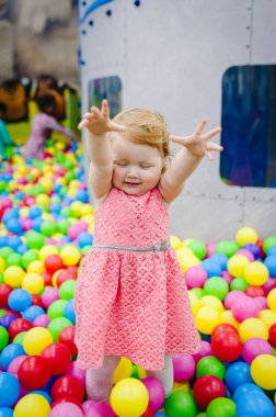 Küçük şirin kız bebek prenses 1-2 yıldır ayakta duruyor ve balonlarla oynuyor, çocuk parkında renkli toplar, top havuzu, doğum günü partisi için kuru havuz. İlk yıl kutlaması konsepti.