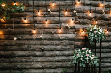 Ahşap duvar süslenmiş çelenkler, parlak ampuller ve süslü çiçeklerle süslenmiş elektrik lambaları. Orijinal düğün çiçeği süsü. Düğün için. Resepsiyon. Salon alanı.