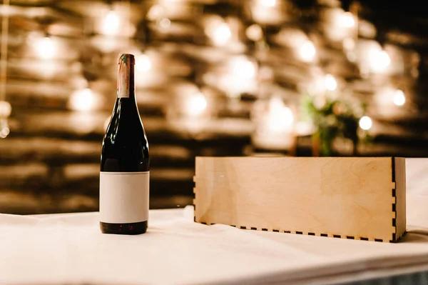 Bottle of wine with label. Mockup. Red wine bottle in wooden box with soft bokeh isolated on lights background. With copy space.