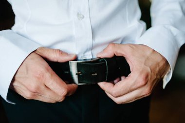 Pantolon ve gömlekli bir adam siyah deri pantolon kemerini ilikledi. Damat kemeri tokayla takar. İş adamı deri kemer takar..
