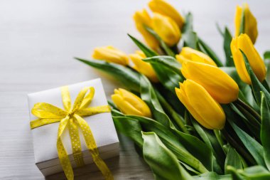 Beyaz kırsal ahşap arka planda hediye kutusu olan sarı laleler. Mesaj için yer var. Sevgililer günü, kadınlar, anneler günü, Paskalya için bayram tebrik kartı. Doğum günü.