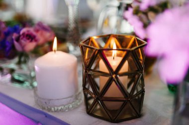 Menekşe, mor, pembe çiçekler ve yeşillik kompozisyonu ile süslenmiş şölen masası, şölen salonunda mumlar. Yeni evliler düğün ziyafeti alanında toplandı..