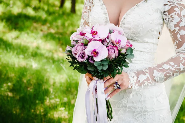 エレガントなドレスの若い美しい女の子が立っており 自然のリボンとパステルピンクの花や緑の手花束を保持しています 花嫁は屋外で結婚式の花束を保持します — ストック写真