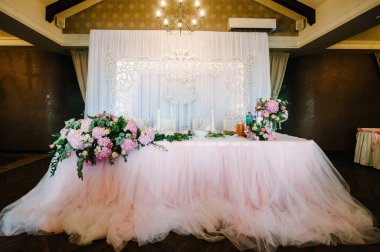 Kutlama masası, menekşe, mor, pembe çiçekler ve yeşillikle süslenmiş kemer, ziyafet salonunda mumlar. Yeni evliler düğün ziyafeti alanında toplandı..