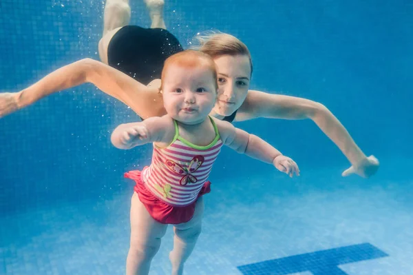 母は娘がプールで水の下で泳いで 水に浸かっている保持しています 潜水赤ちゃん 幼児の水泳を学ぶ 若いですお母さんや水泳インストラクターと幸せな女の子 — ストック写真