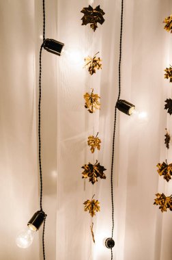 Dry golden leaves, garlands and light bulbs on white background. Gold wedding reception.  Autumn style. Luxury elegant wedding decor for the ceremony.