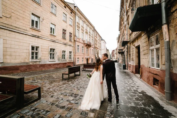 Portrait the groom and the bride going back and kissing near old building, old house outside, outdoor. Newlyweds are walking along the streets of the city of Lviv. Wedding walks.