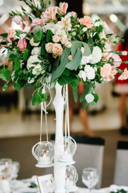 Çiçek ve yeşilden oluşan bir kompozisyon düğün salonundaki şenlik masasında. Mumlar duruyor. Kapat..