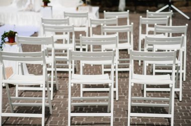 Ahşap beyaz sandalyeler arka bahçedeki ziyafet alanında kurdele ve yeşilliklerle süslenir. Düğün töreni. Yol. Düğün dekoru. Yan görünüm ve dikey görünüm.