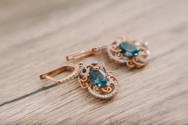 Tahta arka planda elmas küpeler. Mavi kristalli küpeler, mücevherler. Küçük elmaslı iki altın safir küpe. Aquamarine turkuaz topaz değerli taş. Kapat..
