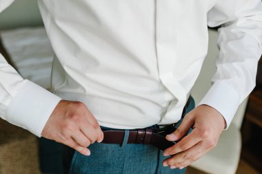 Pantolon ve gömlekli bir adam kahverengi deri pantolon kemerini ilikledi. Damat kemeri tokayla sar. İş adamı deri kemer takar. Yeni klasik kemer.