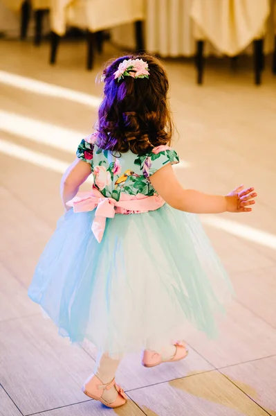 Happy baby girl dancer dancing the modern dance. Little child dancing, jumping, running, having fun. Party dancing concept. Cute girl in a beautiful dress is dancing in a light sunny room. Back view.