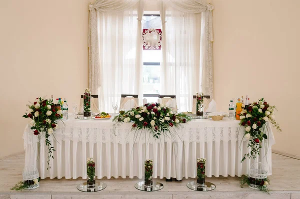 Festive table, arch, stand decorated with a composition of red, white flowers and greenery, candles in the banquet hall. Table newlyweds in the banquet area on wedding party.
