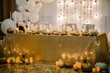 Table setting for wedding. Decorated arch for wedding ceremony. White balloons, candles, autumn leaves and small pumpkins. Autumn location and Halloween decor.