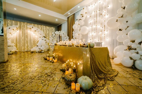 Table setting for wedding. Decorated arch for wedding ceremony. White balloons, candles, autumn leaves and small pumpkins. Autumn location and Halloween decor.