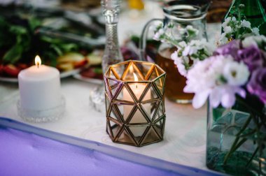 Menekşe, mor, pembe çiçekler ve yeşillik kompozisyonu ile süslenmiş şölen masası, şölen salonunda mumlar. Yeni evliler düğün ziyafeti alanında toplandı..