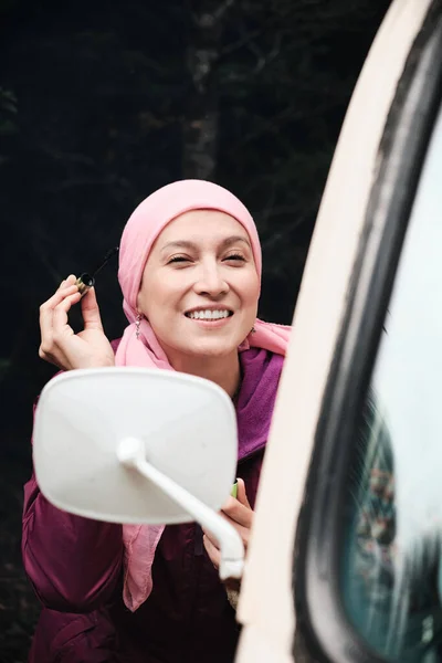 portrait of woman with cancer smiling while looking at herself in the mirror of her car