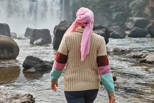Young woman with cancer is on her back in front of a waterfall.