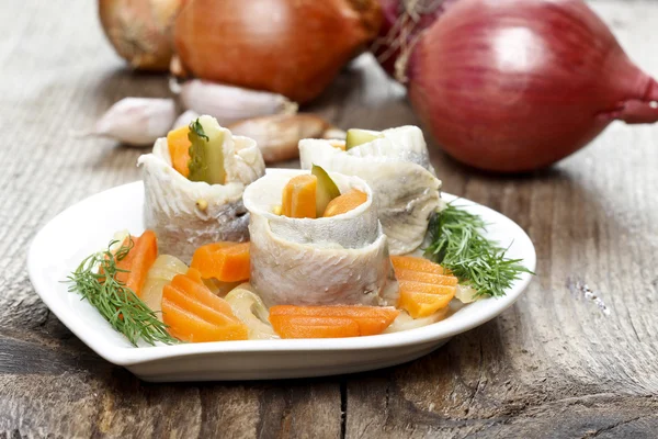 Rollos de arenque en escabeche con verduras en mesa de madera —  Fotos de Stock