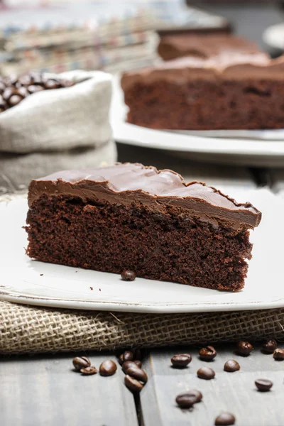 Schokoladenkuchen auf weißem Teller, auf hessisch. Kaffeebohnen auf Holz — Stockfoto