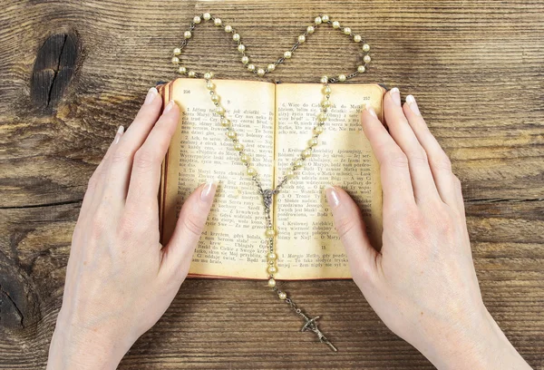 Händerna håller Bibeln och be med ett radband — Stockfoto