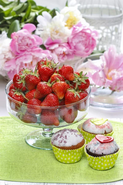 Glazen kom van aardbeien en groene cupcakes op groene servet. — Stockfoto