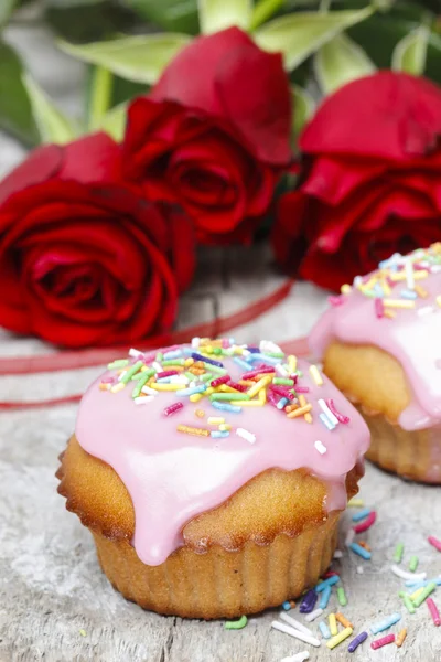 Muffins cobertos com cobertura rosa e polvilhas coloridas em madeira — Fotografia de Stock