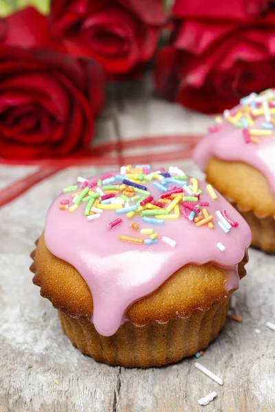 Muffins covered with pink icing and colorful sprinkles on wooden — Stock Photo, Image